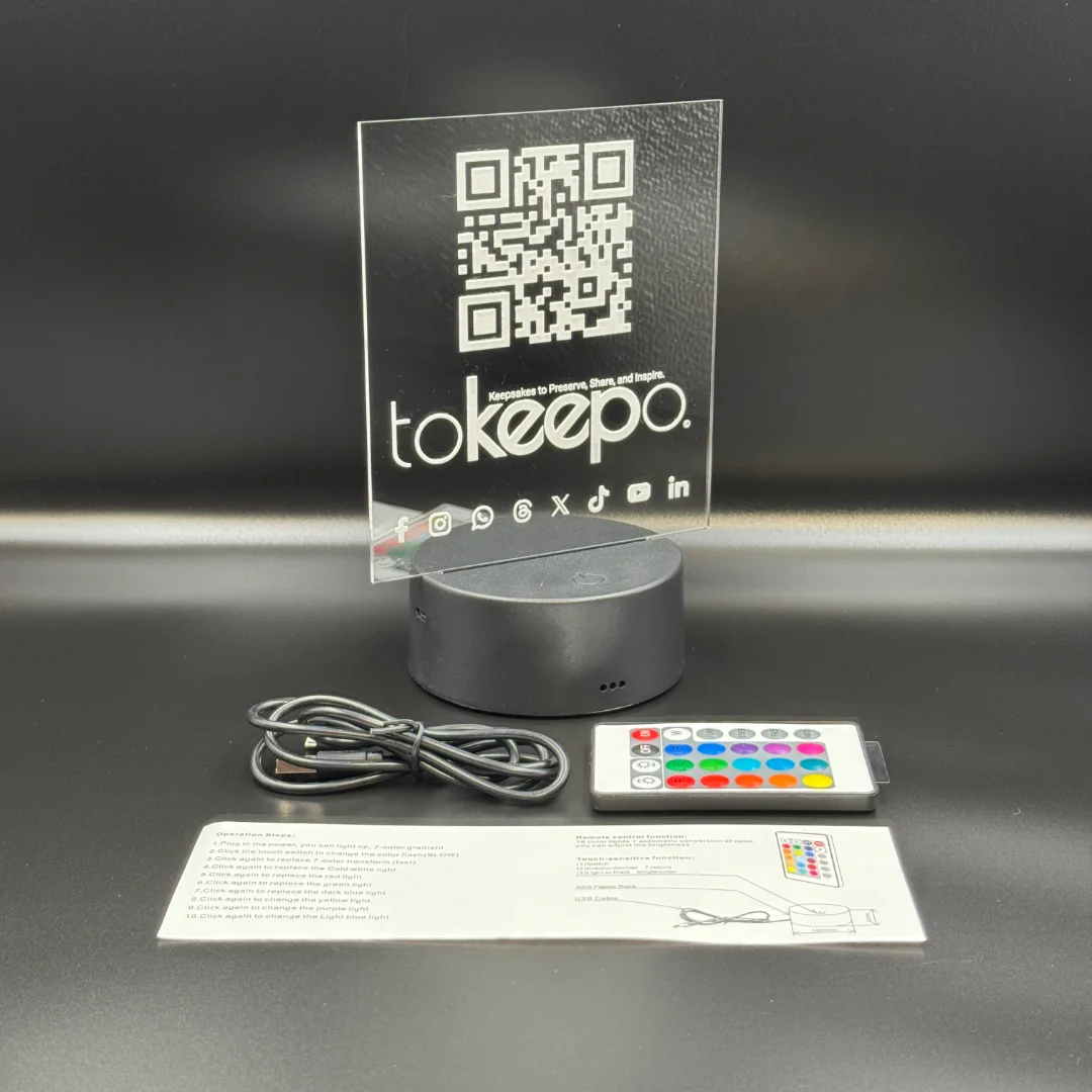 LED Acrylic Desk Lamp by tokeepo with a glowing acrylic plaque featuring engraved designs, including a QR code and logo, illuminated on a laser engraved transparent acrylic. USB cable, remote control, and manual are also in the picture.