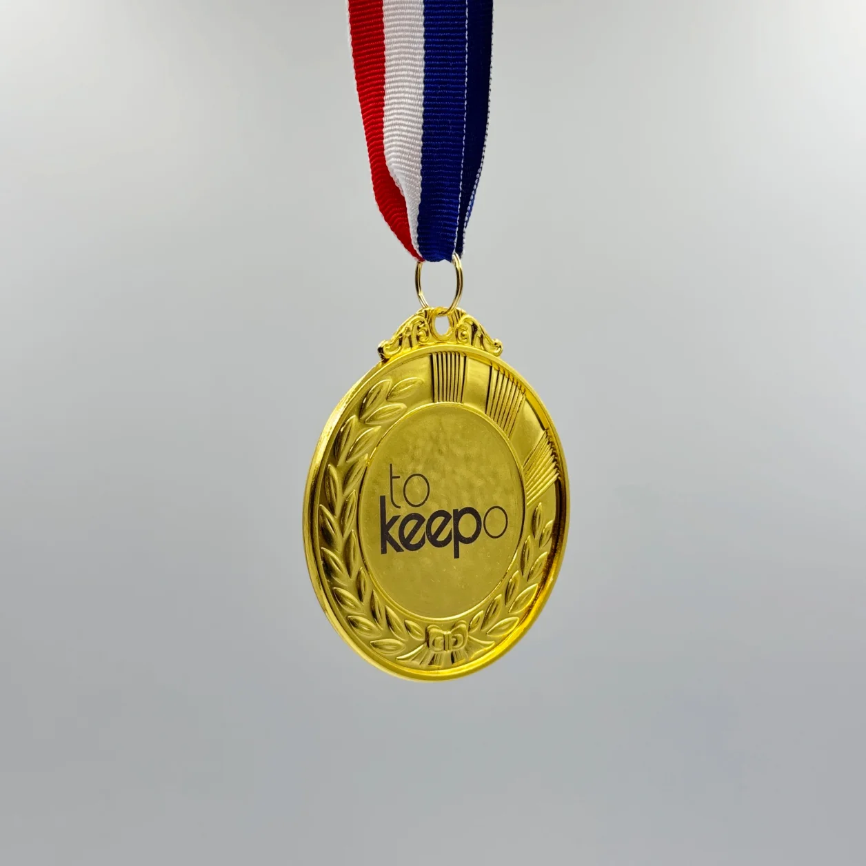 A gold medal with neck ribbon featuring a laurel wreath design, laser marked with the "tokeepo" logo in the center, hanging from a red, white, and blue ribbon.