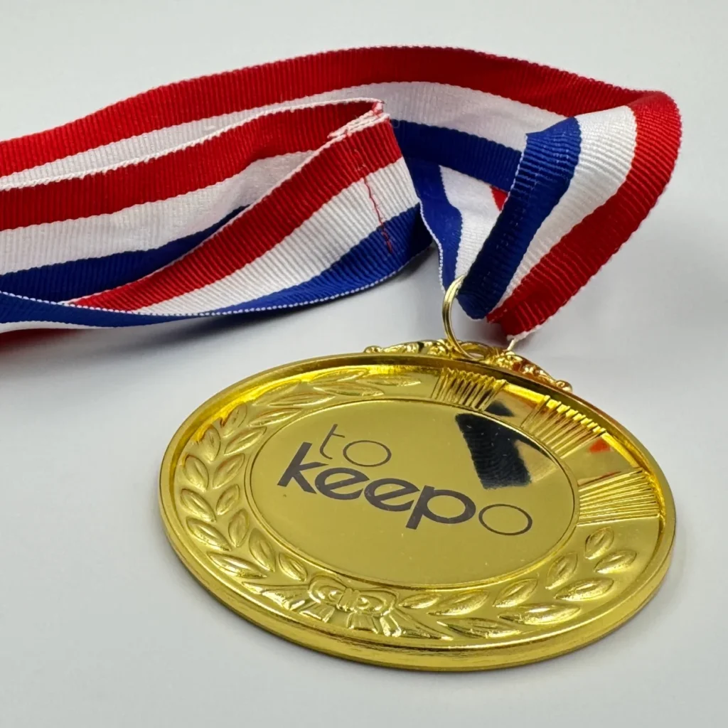 A gold medal with neck ribbon featuring a laurel wreath design, laser marked with the "tokeepo" logo in the center, hanging from a red, white, and blue ribbon.