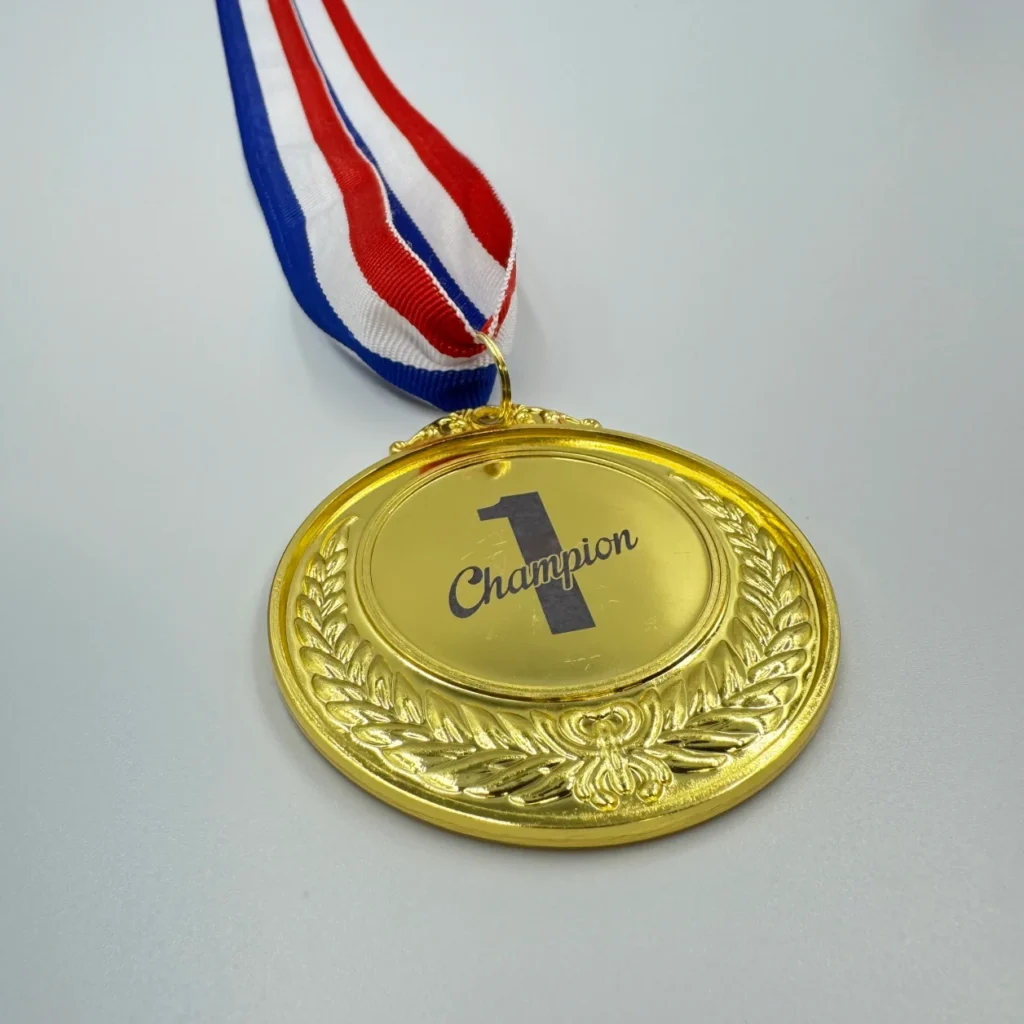 A gold medal with neck ribbon featuring a laurel wreath design, laser marked with the "Champion 1" logo in the center, hanging from a red, white, and blue ribbon.