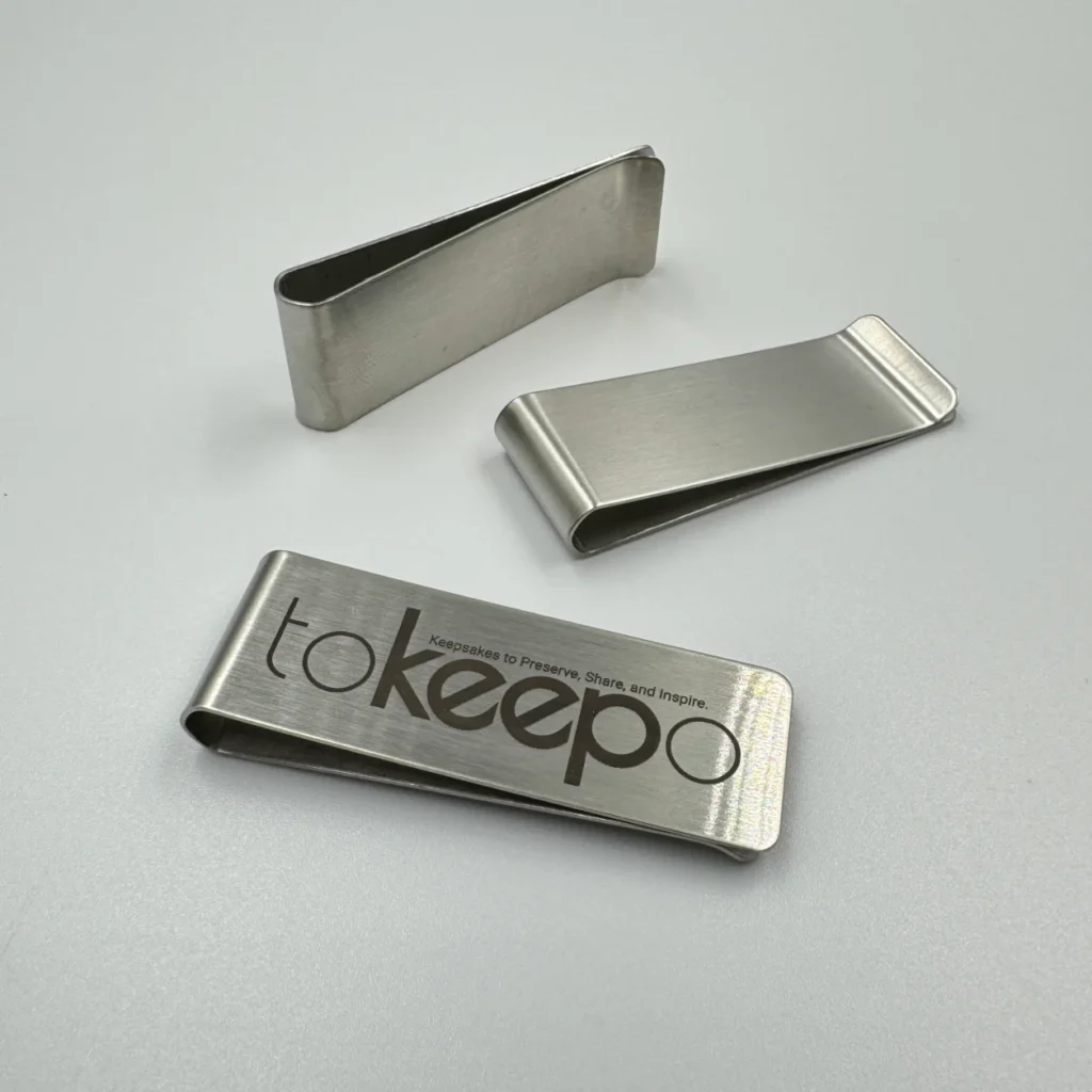 Three stainless steel money clips, engraved with the "tokeepo" logo, on a white surface.