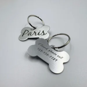 Two stainless steel bone-shaped pet tags, one engraved with the name "Paris" and the other displaying a contact number for lost pet recovery.