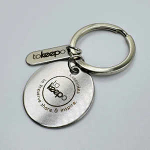 A stainless steel keychain with a circular marked pendant and a small rectangular tag, both featuring the "tokeepo" logo.