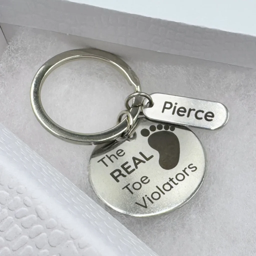 A stainless steel keychain with a circular marked pendant and a small rectangular tag.
