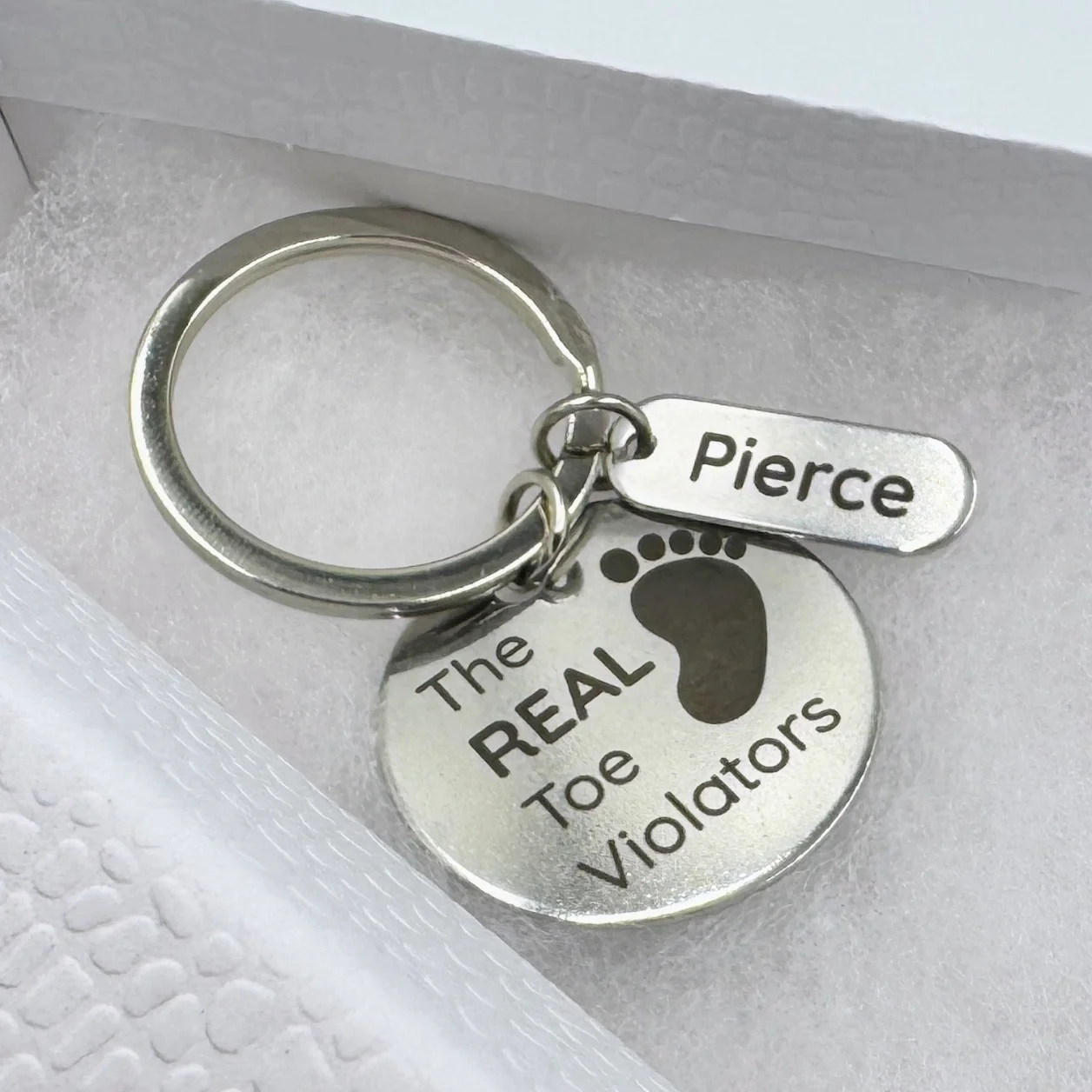 A stainless steel keychain with a circular marked pendant and a small rectangular tag.