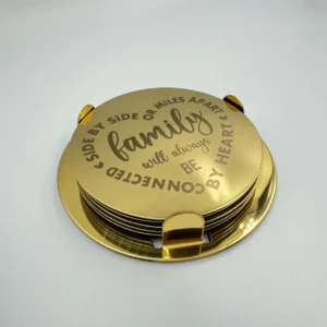A gold stainless steel coaster set with an engraved family quotes, neatly stacked in a matching holder.