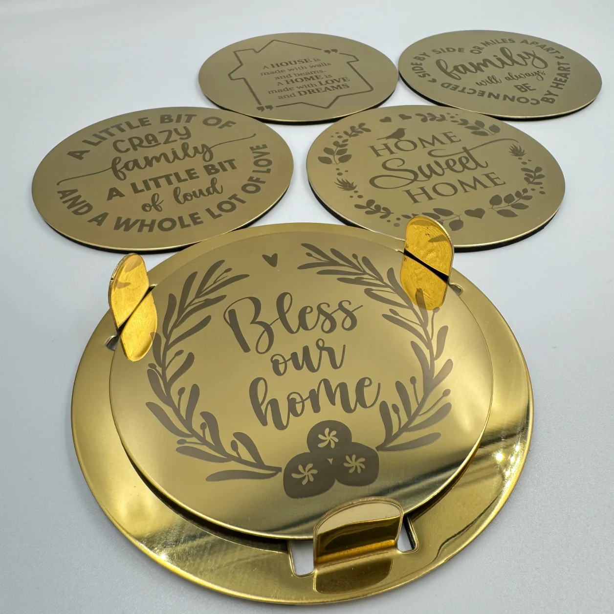 A gold stainless steel coaster set with an engraved family quotes, neatly stacked in a matching holder.