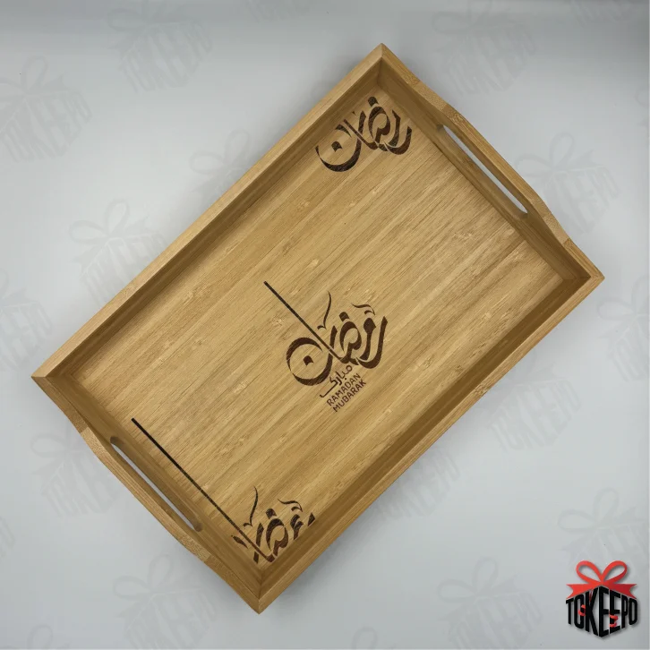 Top view of an empty bamboo serving tray engraved with Ramadan calligraphy and corner motifs.