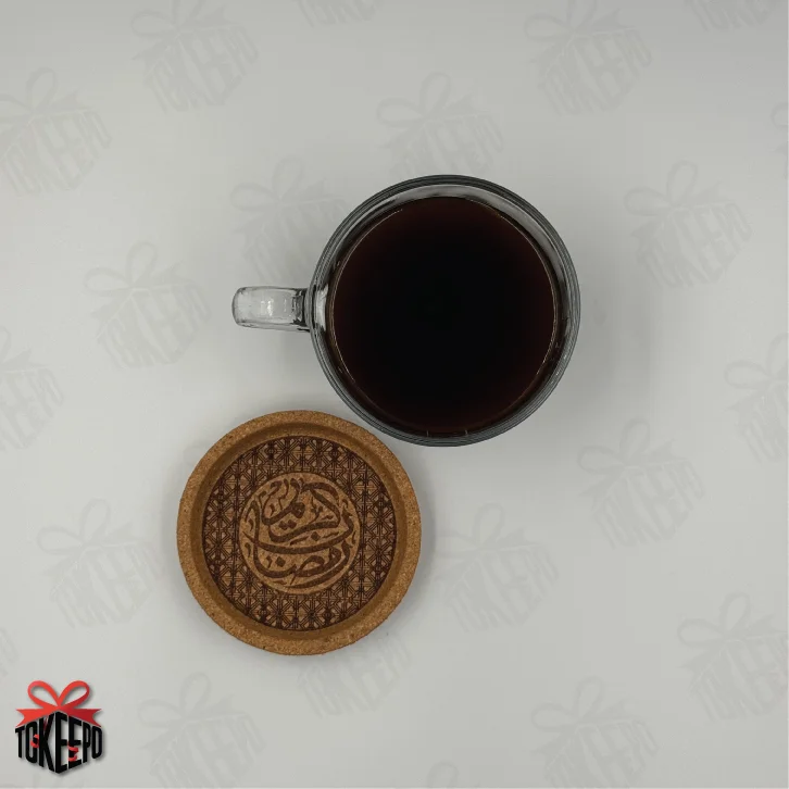 Top view of glass coffee mug and cork coaster laser engraved with Arabic calligraphy and geometric pattern.