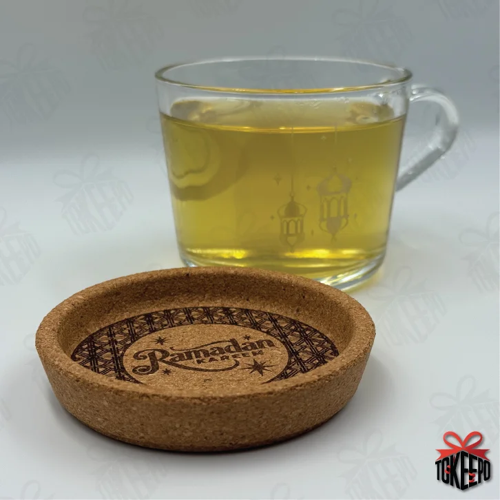 Ramadan cork coaster with “Ramadan” engraving and geometric border, shown beside a glass tea mug.
