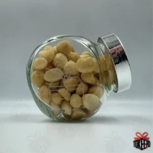 Engraved glass reward jar labeled for Sadaqah/Zakat, filled with macadamia nuts and shown on its side with a silver lid.