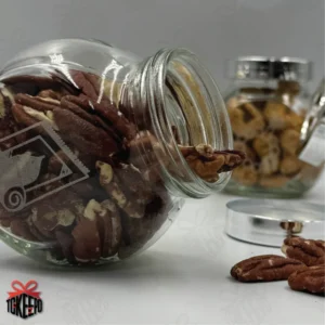 Open engraved Salah reward jar tipped on its side with pecans spilling out, with other jars blurred in the background.